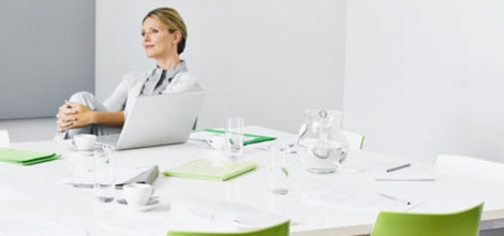 Modern conference room with white table, green chairs and a laptop on the table.