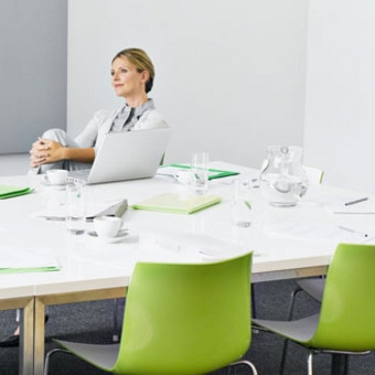 Modern conference room with white table, green chairs and a laptop on the table.