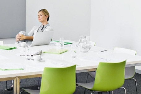 Modern conference room with white table, green chairs and a laptop on the table.