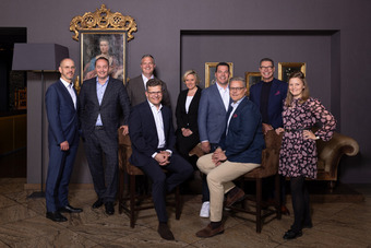 Group photo with the board members of DEHAG Hospitality Group AG: nine people in business attire seated and standing in an elegant room with paintings and an ornate frame.