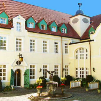 Historisches Gebäude mit Uhrturm, grünen Fensterläden und rotem Ziegeldach – ein charmantes Beispiel regionaler Architektur, ideal als Kulisse für ein traditionsreiches Hotel.
