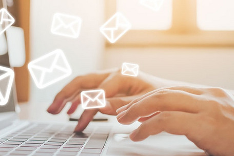 Nahaufnahme von Händen auf einer Tastatur, im Hintergrund Sonnenlicht durch ein Fenster – symbolisiert digitale Kommunikation.