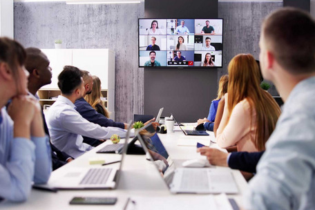 People in a meeting room join a video conference displayed on a large screen