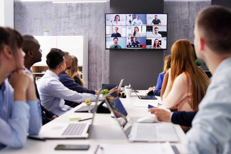 People in a meeting room join a video conference displayed on a large screen