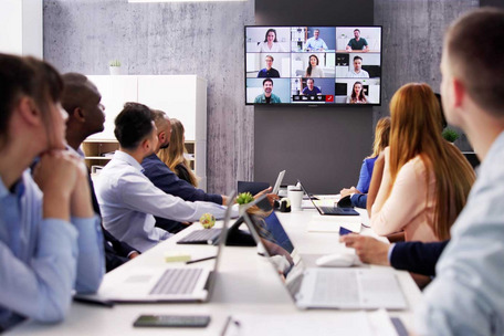 People in a meeting room join a video conference displayed on a large screen