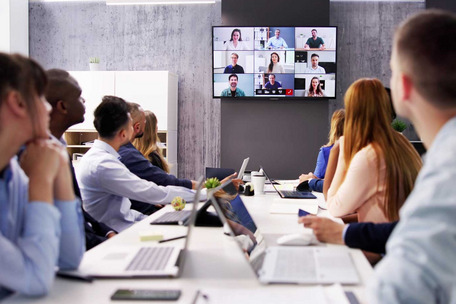 Personen sitzen in einem Konferenzraum und nehmen an einer Videokonferenz mit mehreren Teilnehmenden teil