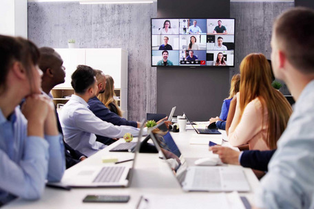 Personen sitzen in einem Konferenzraum und nehmen an einer Videokonferenz mit mehreren Teilnehmenden teil