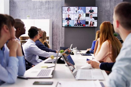 Personen sitzen in einem Konferenzraum und nehmen an einer Videokonferenz mit mehreren Teilnehmenden teil