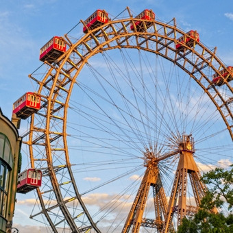 Vienna Ferris wheel in Prater with red cabins against blue sky and trees.