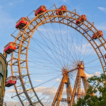 Wiener Riesenrad im Prater vor blauem Himmel mit roten Gondeln und Bäumen.